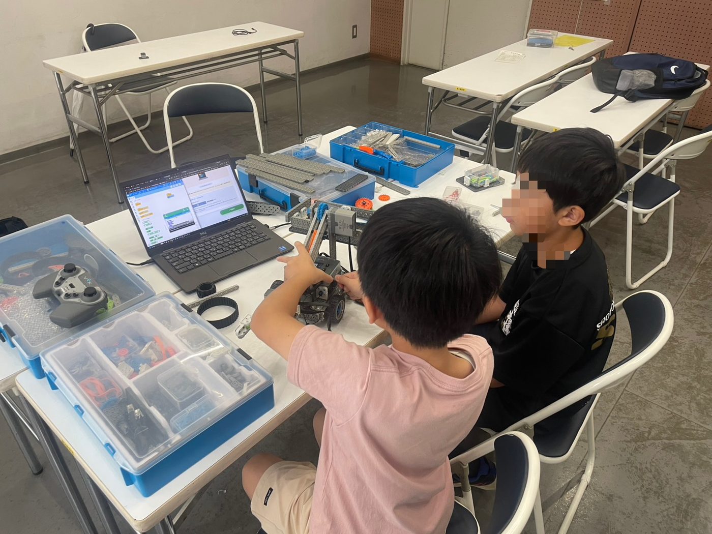 ネコモニNaviを開いたノートパソコンの前で、組み立てたロボットを手に話し合う子どもたち