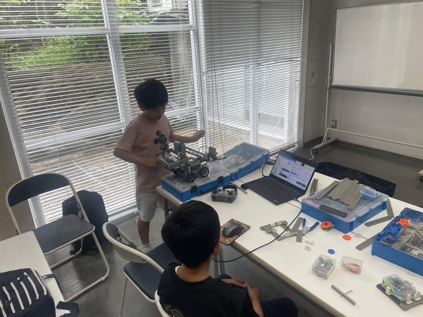 組み立てたロボットを運ぶ様子。机の上にはネコモニNaviを開いたノートパソコンとVEX IQのパーツ